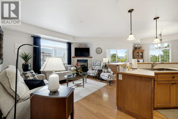 Open-concept living room and kitchen area with wood floors, fireplace, and island. - 611 Shuswap Street Sw Unit# 301, Salmon Arm