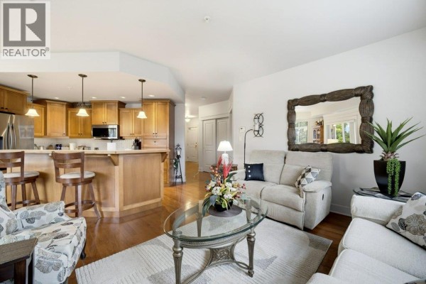 Living room with sofas, armchairs, coffee table, and a kitchen with wood cabinets and island. - 611 Shuswap Street Sw Unit# 301, Salmon Arm