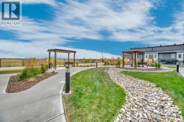 Outdoor common area with manicured lawns, stone pathways, wooden pergolas with benches, and lampposts. - 6112, 200 Seton Circle Se, Calgary