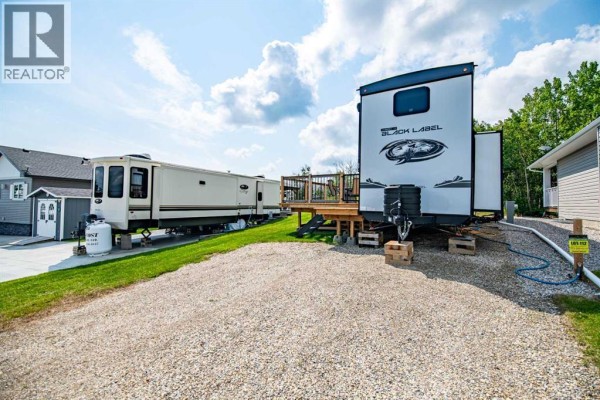Two RVs parked on gravel pads with a backdrop of green grass and trees. - 6112, 25054 South Pine Lake Road, Rural Red Deer County