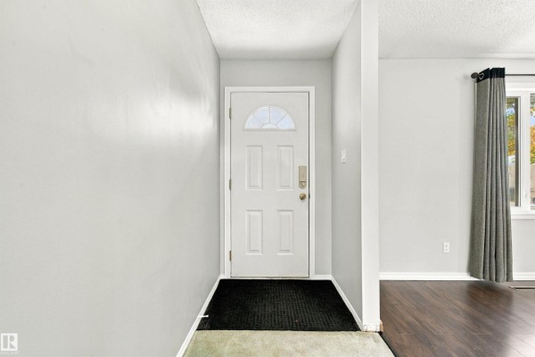 Interior view of a home entrance with a white door, grey walls, and a black doormat. - 6116 148 Av Nw, Edmonton