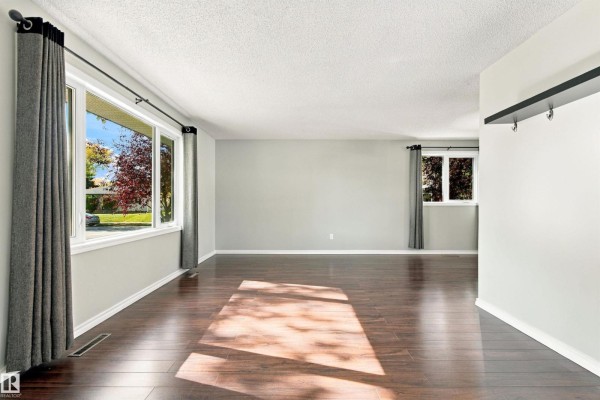 Living room with dark wood floors, grey walls, large windows with dark curtains, and sunlight streaming in. - 6116 148 Av Nw, Edmonton