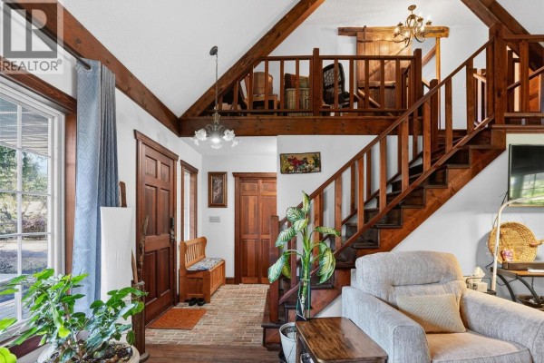 Wooden staircase with railing leading to a living room with vaulted ceilings and exposed beams. - 6119 Pippers Lane, Nelson