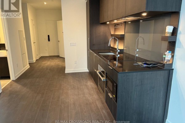 Modern kitchen with dark wood cabinets, stainless steel appliances, and a dark countertop. - 612 - 28 Ann Street, Mississauga