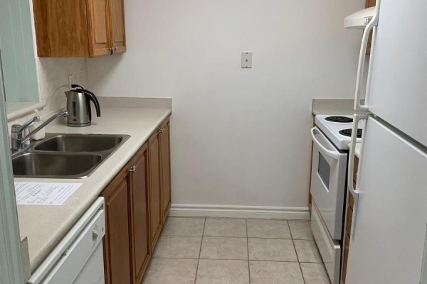 Compact kitchen with light-colored countertops, wooden cabinets, stainless steel sink, and white appliances. - 612 - 3088 Kennedy Road, Toronto