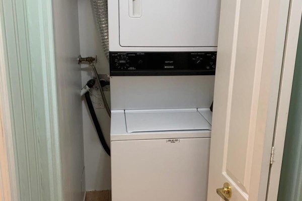 Stacked white front-loading washer and dryer inside a closet with a white door. - 612 - 3088 Kennedy Road, Toronto