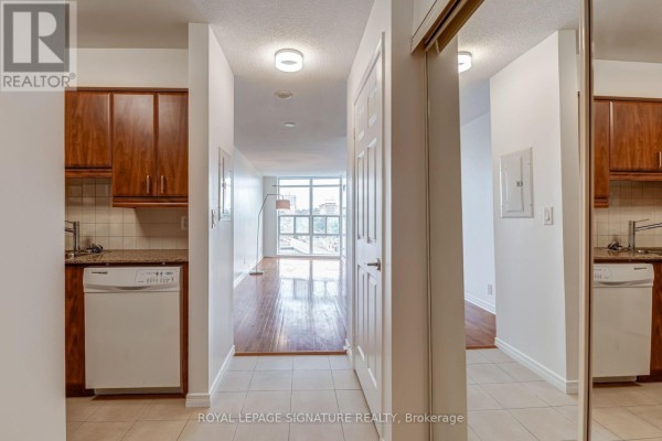 Hallway with beige tile floors, wood cabinets, white appliances, and view into living room. - 612 - 736 Spadina Avenue, Toronto