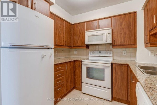 Kitchen with wood cabinets, white appliances including refrigerator, oven, and dishwasher. - 612 - 736 Spadina Avenue, Toronto
