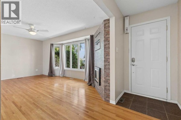Living room with hardwood floors, a bay window with grey curtains, and a decorative stone fireplace. - 612 Mcintosh Road Ne, Calgary