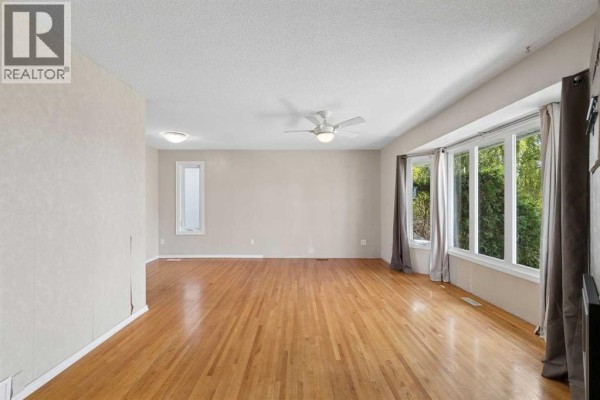 Spacious living room with hardwood floors, large bay windows, and a ceiling fan. - 612 Mcintosh Road Ne, Calgary