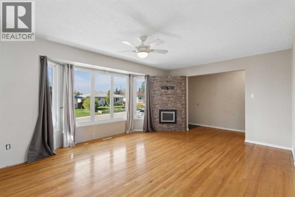 View of the living room and entryway, featuring hardwood floors, bay windows, and a stone accent wall with fireplace. - 612 Mcintosh Road Ne, Calgary