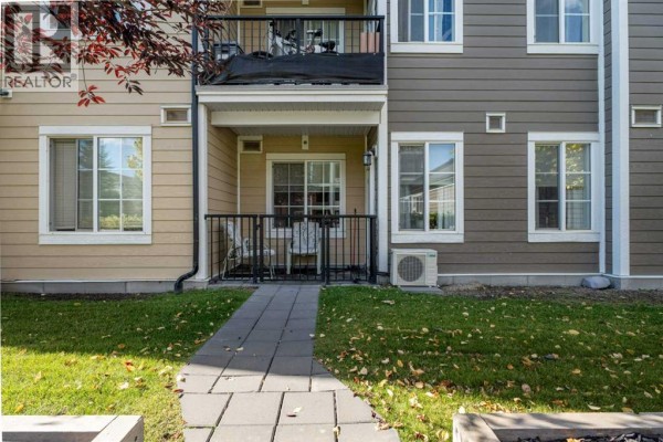Ground floor patio area with grass, stone pathway, and exterior of beige and grey townhome buildings. - 6121, 151 Legacy Main Street Se, Calgary