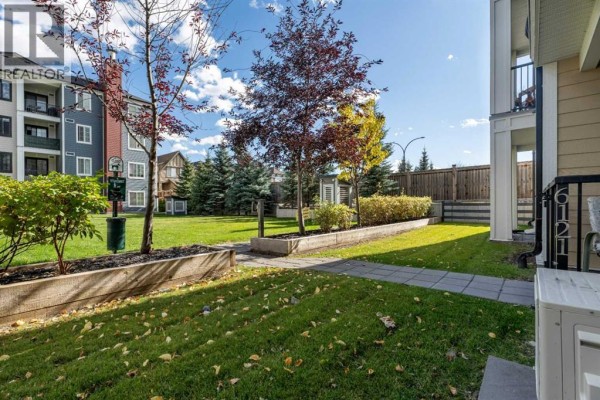 Grassy area with trees and landscaped beds, pathway leading towards townhome buildings with balconies. - 6121, 151 Legacy Main Street Se, Calgary