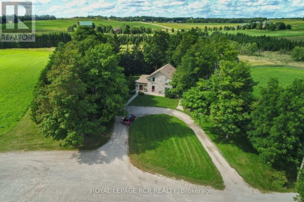Aerial view of the stone house surrounded by mature trees and green fields, with a gravel driveway. - 6122 Ninth Line, Erin