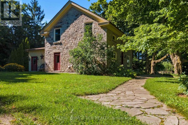 Close-up of the stone farmhouse exterior with multiple windows and a flagstone walkway. - 6122 Ninth Line, Erin
