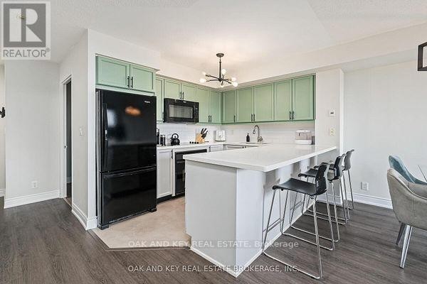 Kitchen with light green cabinets, white countertops, black appliances, and a breakfast bar with stools. - 613 - 245 Davisville Avenue, Toronto