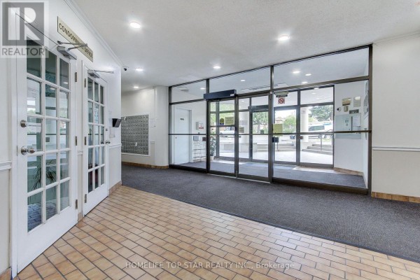 Interior view of the condominium lobby with beige tiled floor, glass doors, and mailboxes. - 613 - 5580 Sheppard E Avenue, Toronto