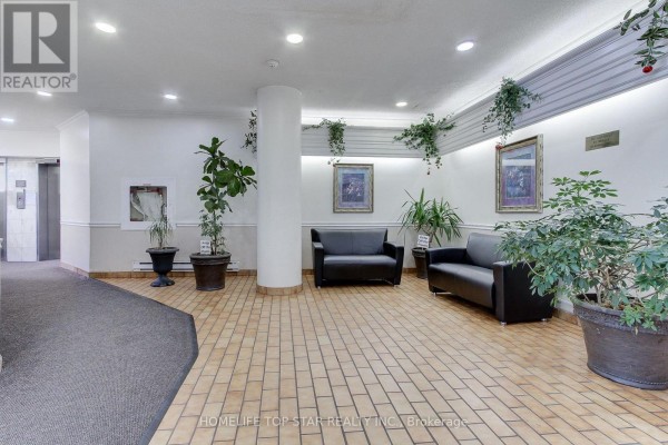 Condominium lobby with black leather sofas, potted plants, and beige tiled flooring. - 613 - 5580 Sheppard E Avenue, Toronto