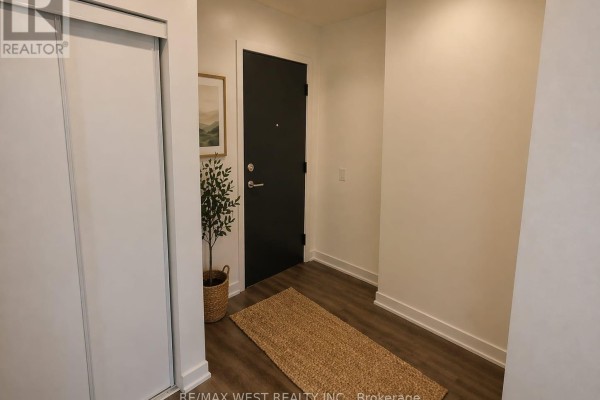 Apartment entryway with a dark grey door, closet, and wood-look flooring with a woven rug. - 614 - 1808 St Clair Avenue W, Toronto