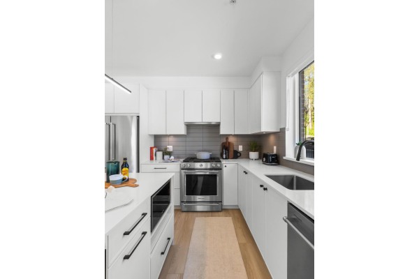 Bright white kitchen with stainless steel appliances, island, and a view of trees. - 614 2771 Montrose Avenue, Abbotsford