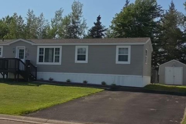 Close-up view of the dark wood front deck and stone walkway with landscaping. - 614 Champlain, Shediac