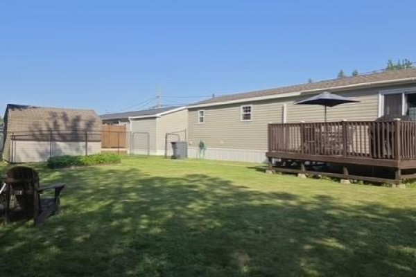 View down the stone walkway and side of the mobile home toward the fenced backyard. - 614 Champlain, Shediac