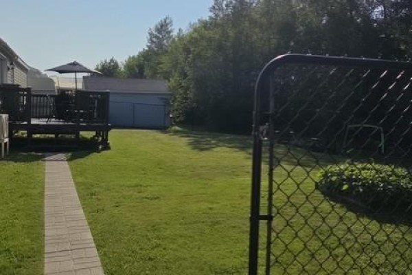 Fenced backyard with a raised garden bed, chairs, and a shed under a blue sky. - 614 Champlain, Shediac