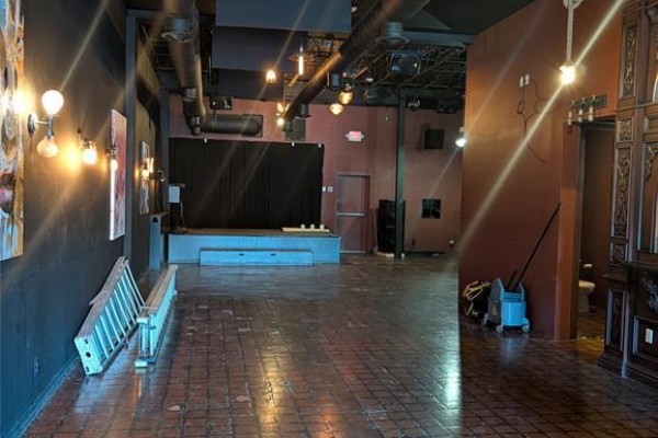 Wide view of a commercial space with a stage, exposed ductwork, and dark walls. - 614 Erie Street East, Windsor
