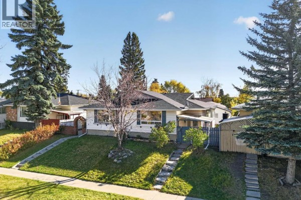 Aerial view of a white bungalow with manicured lawn, mature trees and paved driveway. - 614 Marlborough Way Ne, Calgary