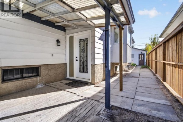 Covered patio area with concrete floor, wooden deck, and a white front door. - 614 Marlborough Way Ne, Calgary