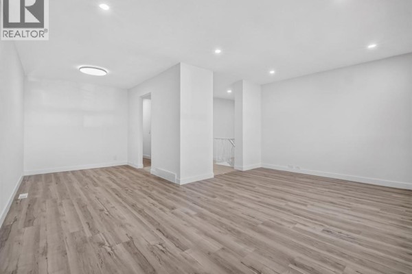 Bright, empty living room with light wood laminate flooring and recessed lighting. - 614 Marlborough Way Ne, Calgary