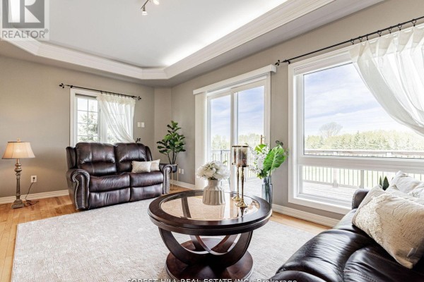 Living room with a leather sofa, large windows, a coffee table, and hardwood floors. - 614 Mcbean Avenue N, Newmarket
