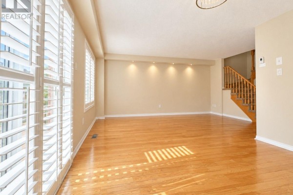 Empty living room with hardwood floors, large windows, and stairs leading up. - 6143 Snowy Owl Crescent, Mississauga