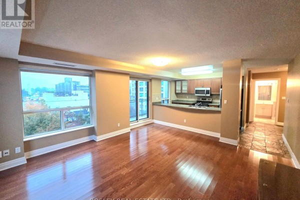 Wide view of the living room and kitchen area, featuring hardwood floors, neutral walls, and tile flooring in the hallway. - 615 - 188 Doris Avenue, Toronto