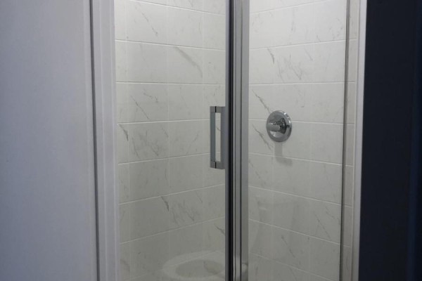 Glass-enclosed shower with white marble-patterned tile and chrome fixtures. - 615 - 2433 Dufferin Street, Toronto
