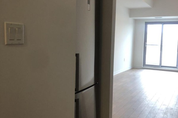 Stainless steel refrigerator next to a light-colored wall, opening to a living area with sliding doors. - 615 - 2433 Dufferin Street, Toronto