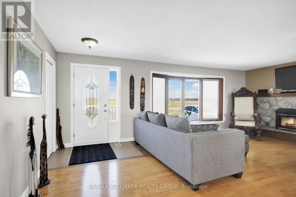 Living room with a large bay window, stone fireplace, television, and a grey sectional sofa. - 6151 Malakoff Road, Ottawa