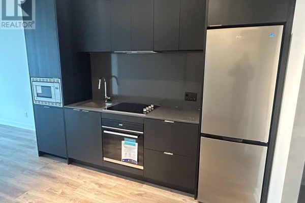 Compact kitchen with dark cabinetry, stainless steel appliances, and light wood laminate flooring. - 616 - 101 John Street N, Hamilton