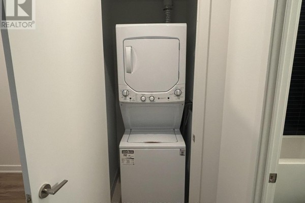 Stacked white washing machine and dryer unit inside a closet with white doors. - 616 - 101 John Street N, Hamilton