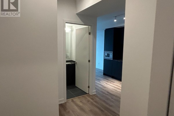 Hallway view looking towards an open doorway revealing a powder room and a dark kitchen. - 616 - 101 John Street N, Hamilton
