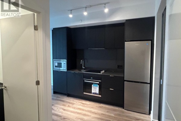 View of a modern apartment kitchen with dark cabinets, stainless steel refrigerator, and microwave. - 616 - 101 John Street N, Hamilton