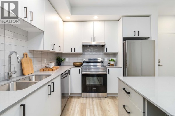 White kitchen with grey tiled backsplash, stainless steel appliances, and quartz countertops. - 617 2390 City Gate Blvd, Langford
