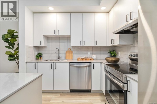 View of a white kitchen with stainless steel refrigerator, oven, and modern cabinetry. - 617 2390 City Gate Blvd, Langford