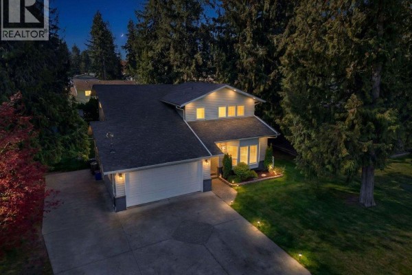 Aerial nighttime view of the light blue house with illuminated windows and landscaping. - 617 Pine Street, Sicamous