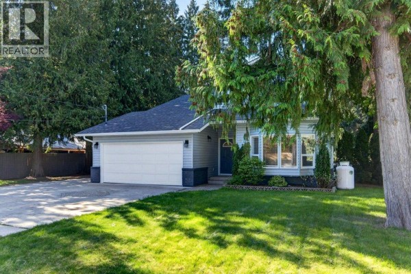 Close-up of the house entrance with a bay window, lawn, and propane tank. - 617 Pine Street, Sicamous