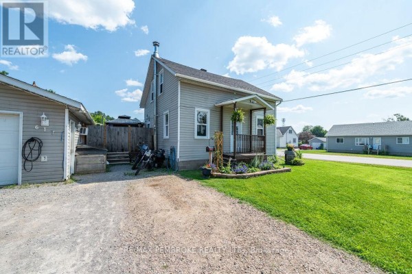 Side view of the house, highlighting the beige siding, windows, and the entrance porch with potted plants. - 617 Third Avenue S, Laurentian Valley