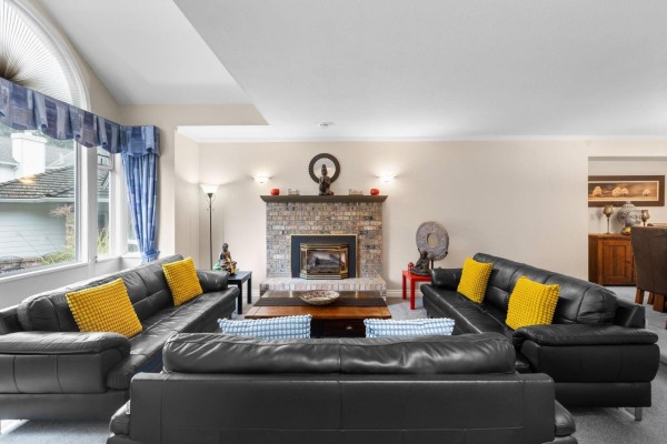 Living room with black leather sofas, a brick fireplace, and a large arched window. - 6173 Parkside Court, Surrey