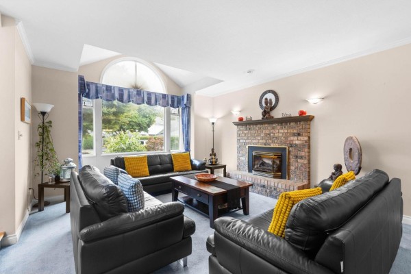 Living room with a brick fireplace, large arched window, and multiple seating areas. - 6173 Parkside Court, Surrey