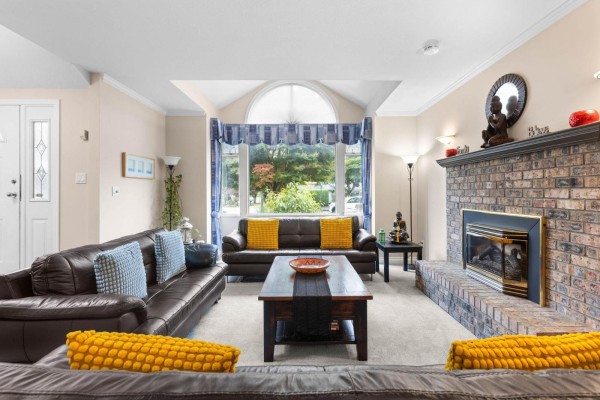 Spacious living room with a brick fireplace, large window, and seating arranged around a coffee table. - 6173 Parkside Court, Surrey