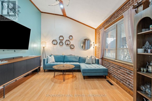 Living room featuring a blue sectional sofa, wooden floors, and exposed brick wall - 618 Lincoln Street, Welland